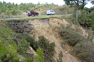 Picture shows a slip on the side of the hill while cars drive along the road on top of the hill