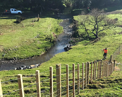 Image of a man carrying wooden fence posts across a creak