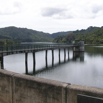 A wooden jetty extending over a calm reservoir, with hills in the background.