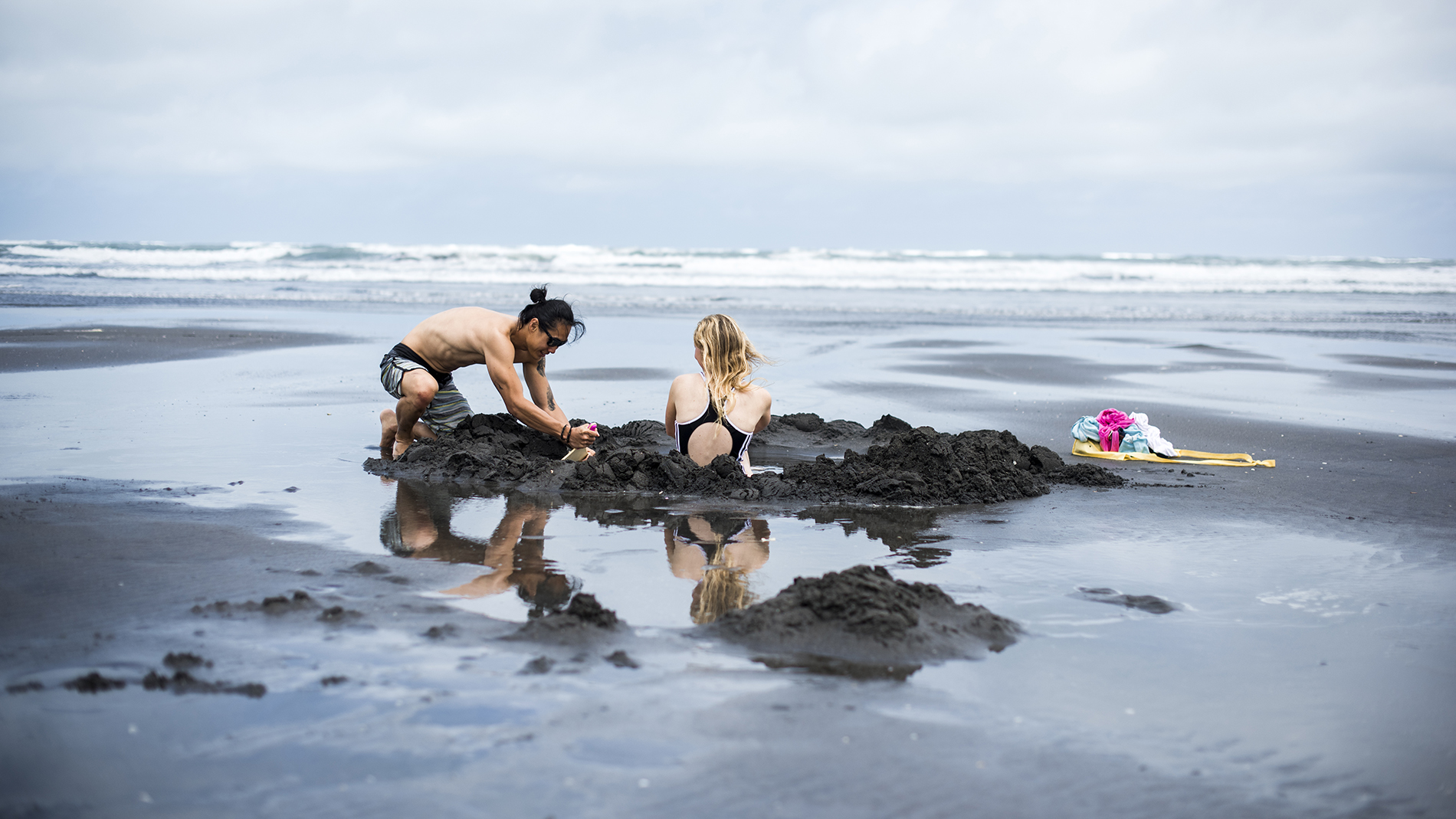 Photo of two people digging a bathing hole on hot water beach