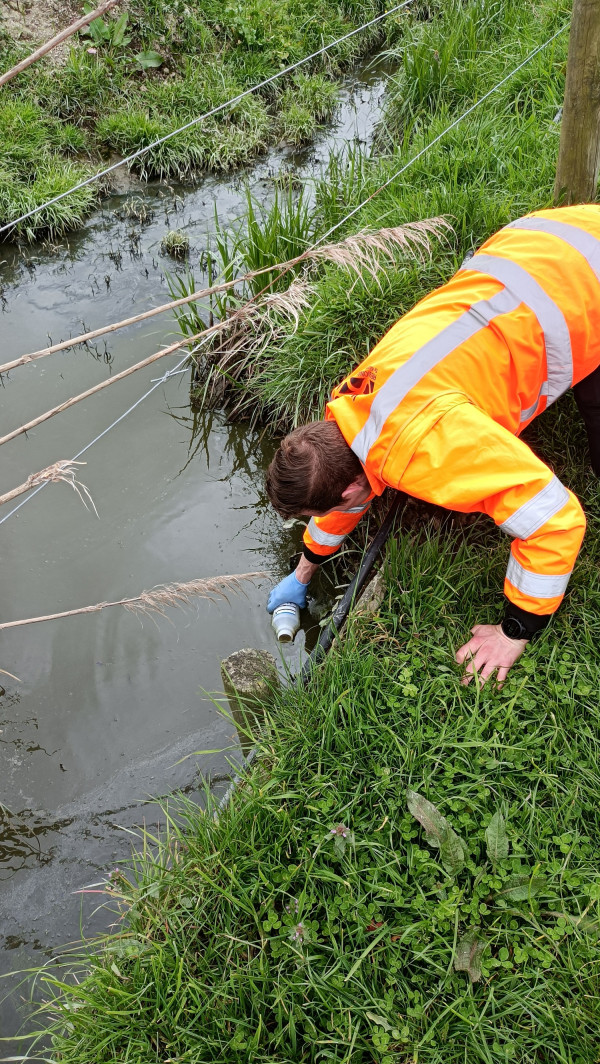 Image of someone taking a water sample from a flooded field